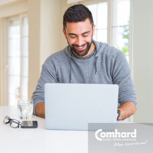 Ein Mann sitzt lächelnd vor einem Laptop.