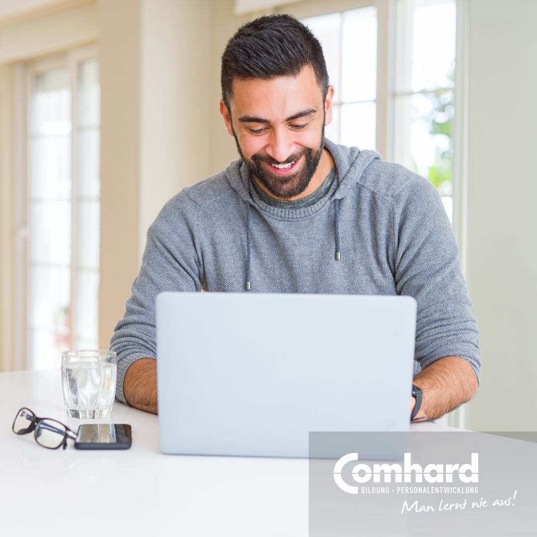 Ein Mann sitzt lächelnd vor einem Laptop.
