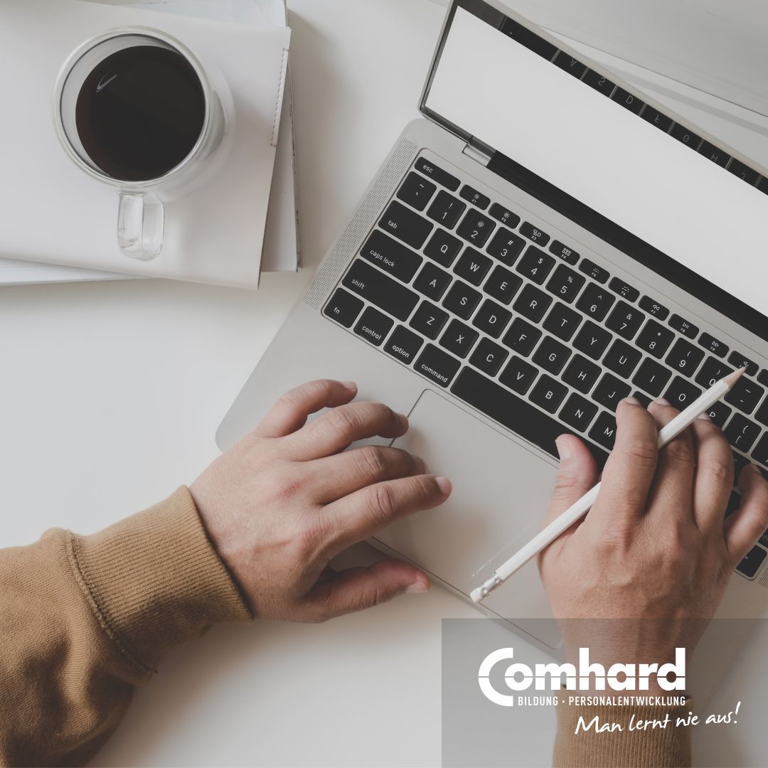 Ein Laptop in der Draufsicht. Man sieht zwei Hände über der Tastatur. Die rechte Hand hält einen Stift. Neben dem Laptop steht ein Kaffee.