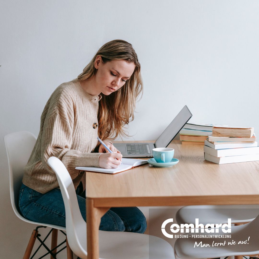 Eine FRau sitzt konzentriert vor einem Laptop und schreibt etwas mit einem Stift in ein Notizbuch