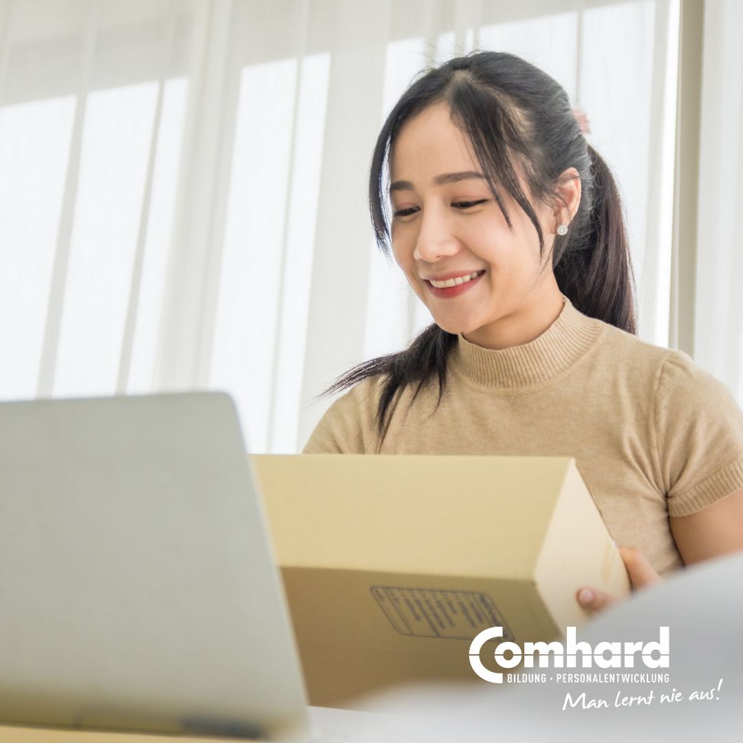Eine Frau sitzt vor einem Laptop und hat ein Paket in der Hand