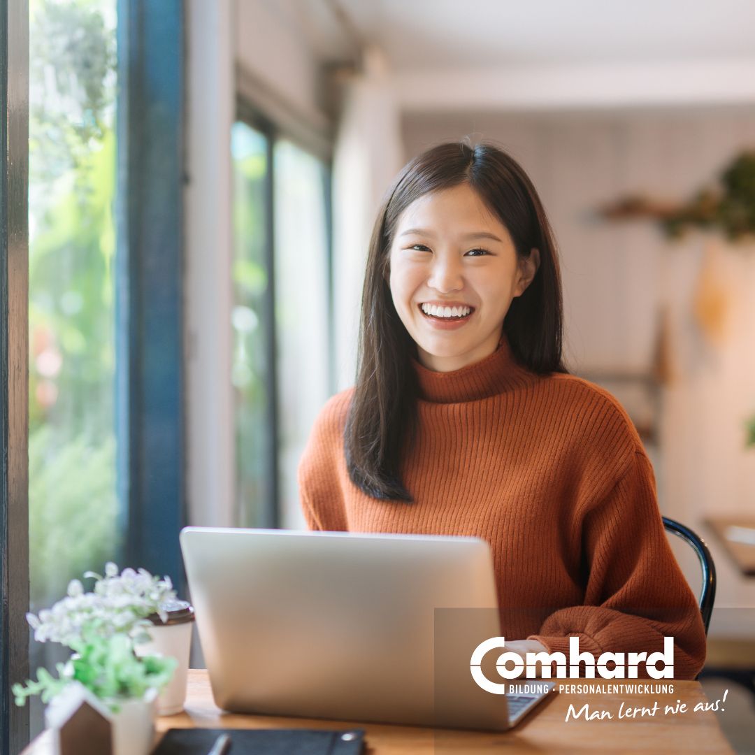 Frau sitzt vor einem Laptop und lächelt in die Kamera