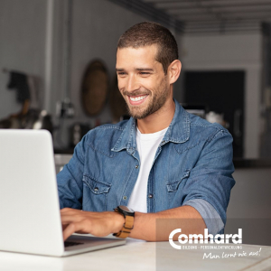 Ein Mann sitzt lächelnd vor einem Laptop.