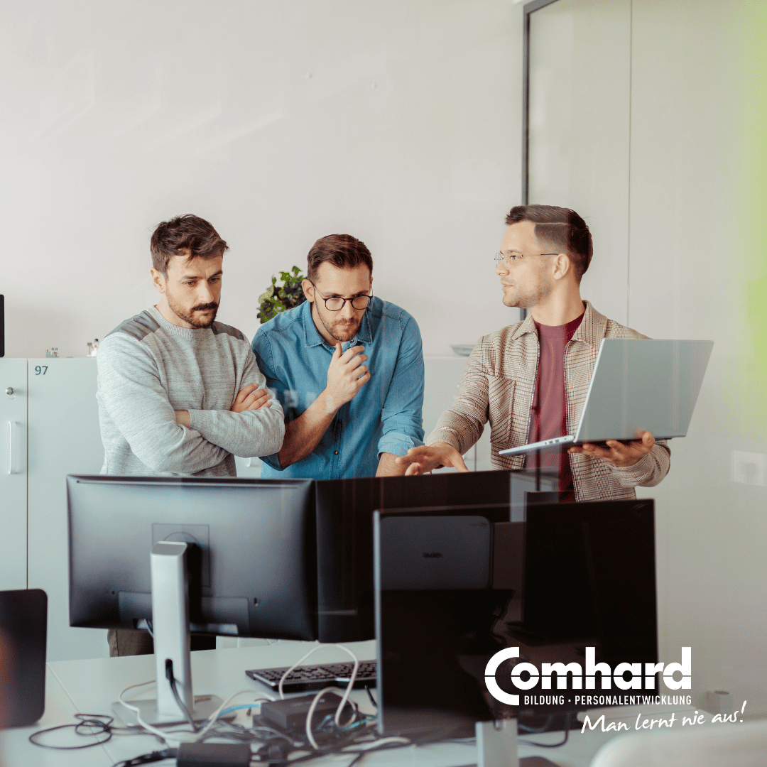 Drei Männer stehen gemeinsam an einem Arbeitsplatz mit mehreren Monitoren und einem Laptop und besprechen digitale Arbeitsinhalte. Das Bild steht für Personalsachbearbeitung, digitale Zusammenarbeit sowie die Arbeit mit DATEV und SAP.