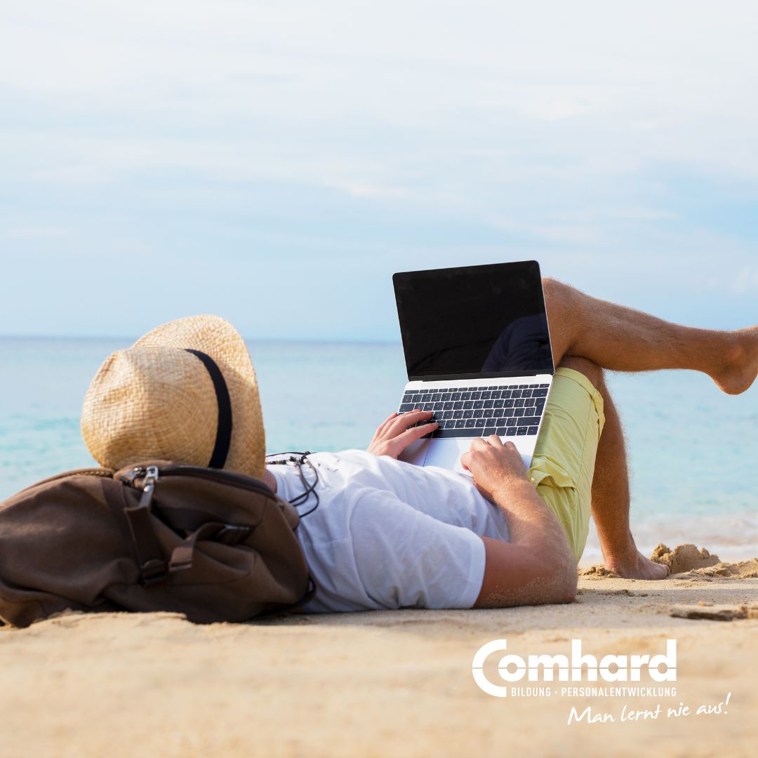 Ein Mann liegt an einem Strand und hat einen Laptop auf seinem Schoß
