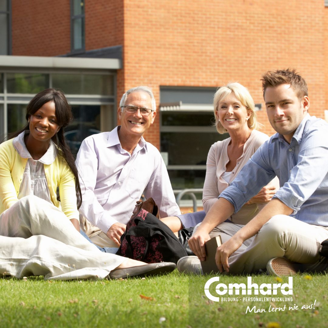 Vier Personen sitzen auf einer Wiese vor einem Gebäude und lächeln.
