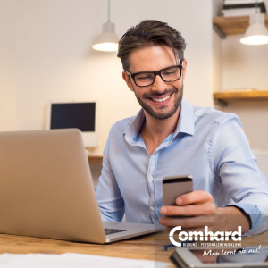 Ein Mann sitzt vor einem Laptop und schaut daneben glücklich auf ein Smartphone.