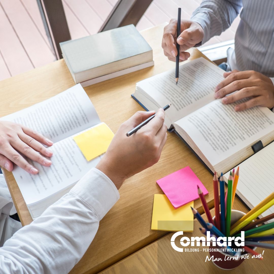 Zwei Personen arbeiten mit Stiften in aufgeschlagenen Büchern.