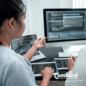 Zwei Personen besprechen Programmiercode an einem Computer und Laptop während der Vorbereitung auf eine IT-Umschulung.