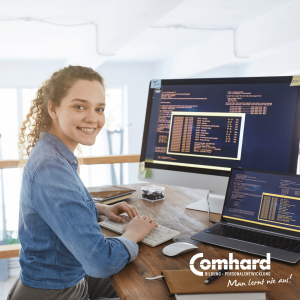 Junge Frau an einem Arbeitsplatz mit Computer und Laptop, auf deren Bildschirmen Programmiercode zu sehen ist. Unten rechts befindet sich das Comhard-Logo.