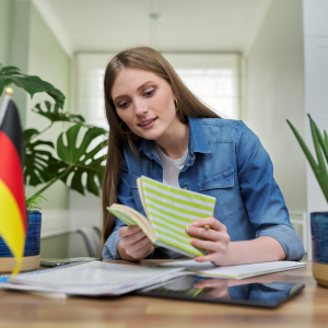 Frau sitzt an einem Tisch mit Dokumenten und schlägt ein Notizbuch auf.